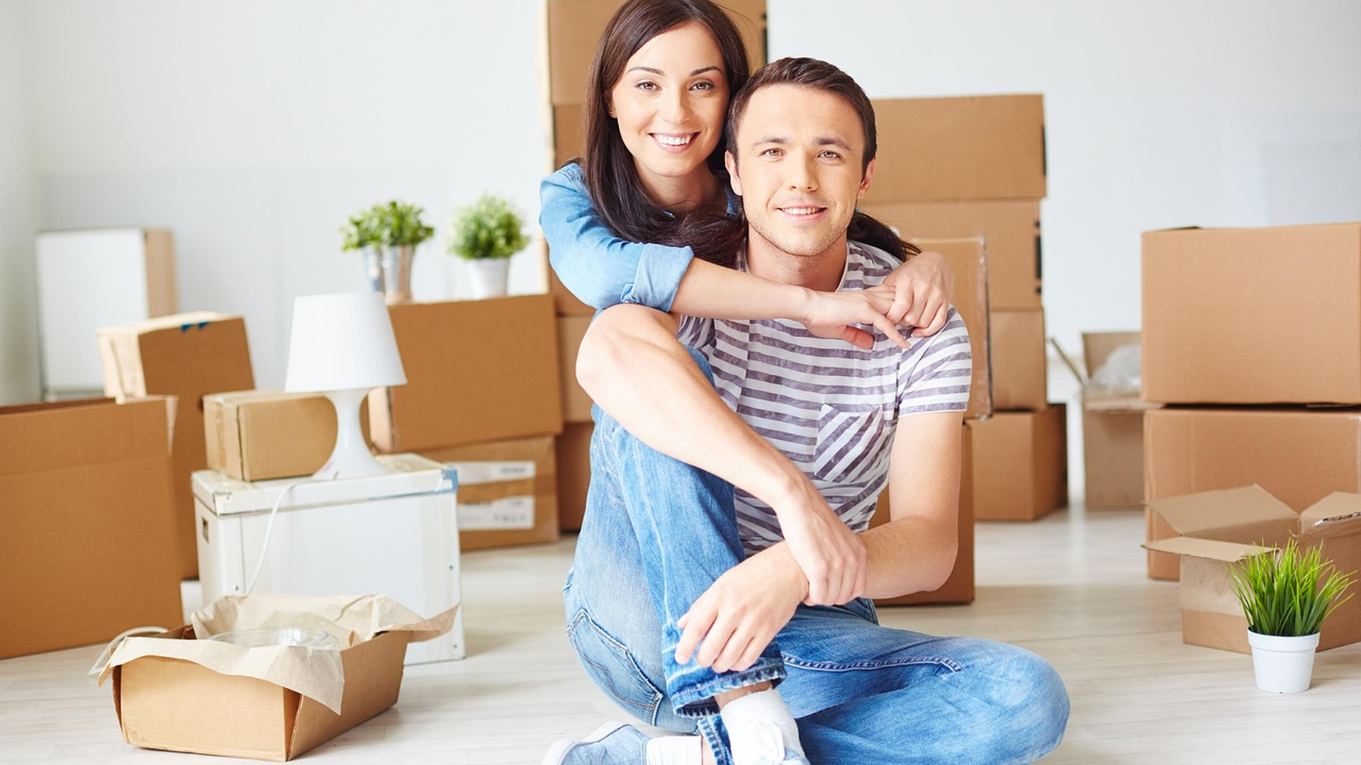 Young couple sitting among moving boxes in their new home after closing on a mortgage with less than 20 percent down