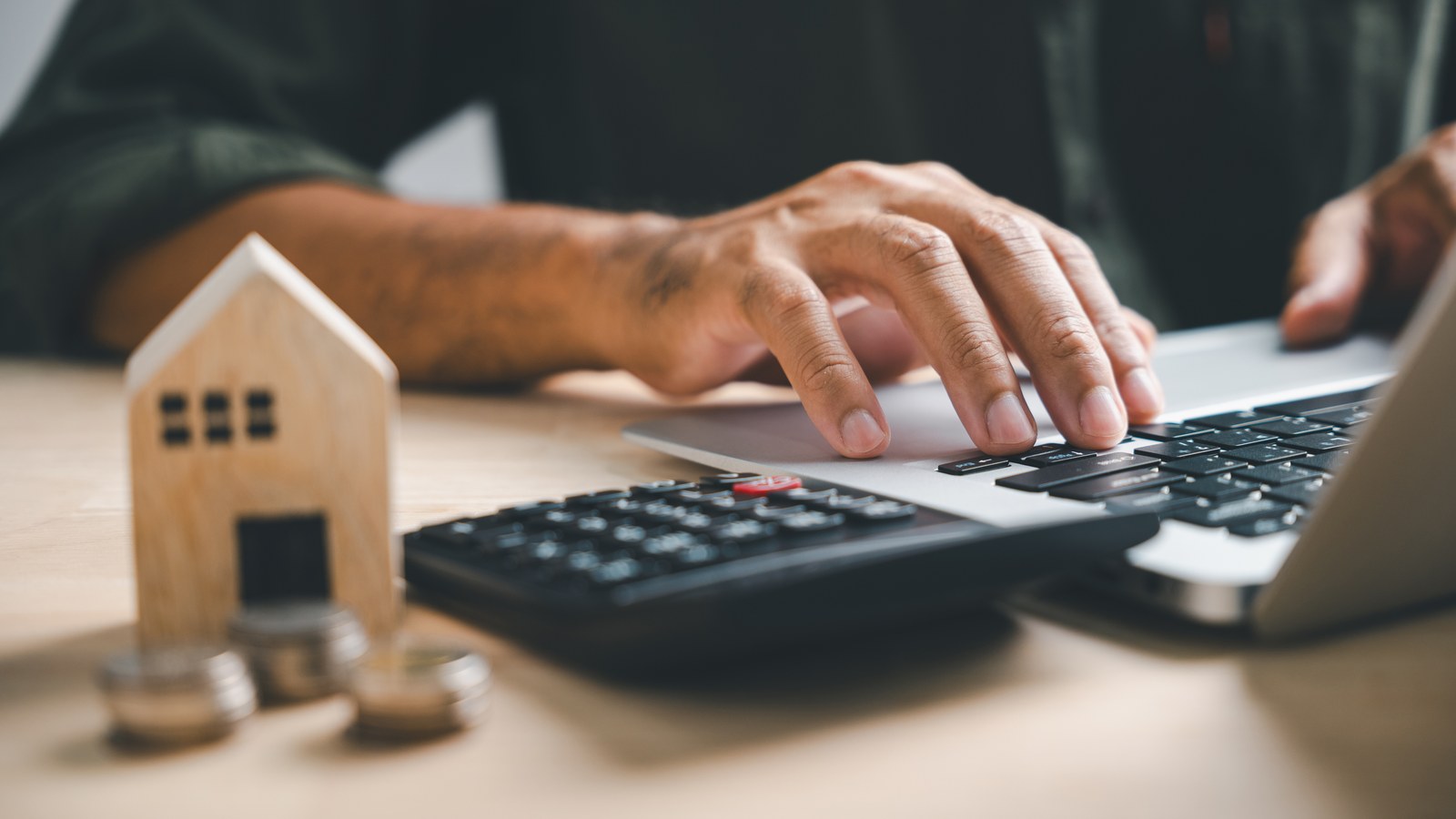 Hand using a calculator beside a model house while comparing rent versus buy costs