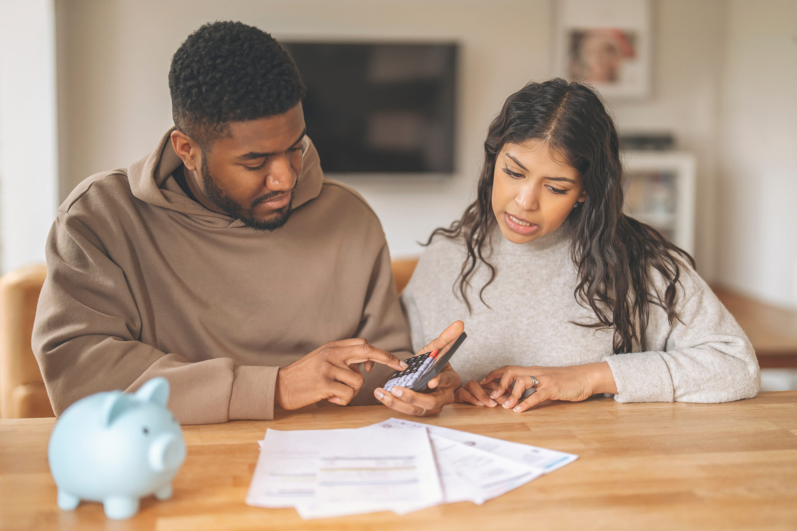 Young couple at a home table using a calculator to figure household finances, the moment many borrowers ask how much house they can actually afford on their income.