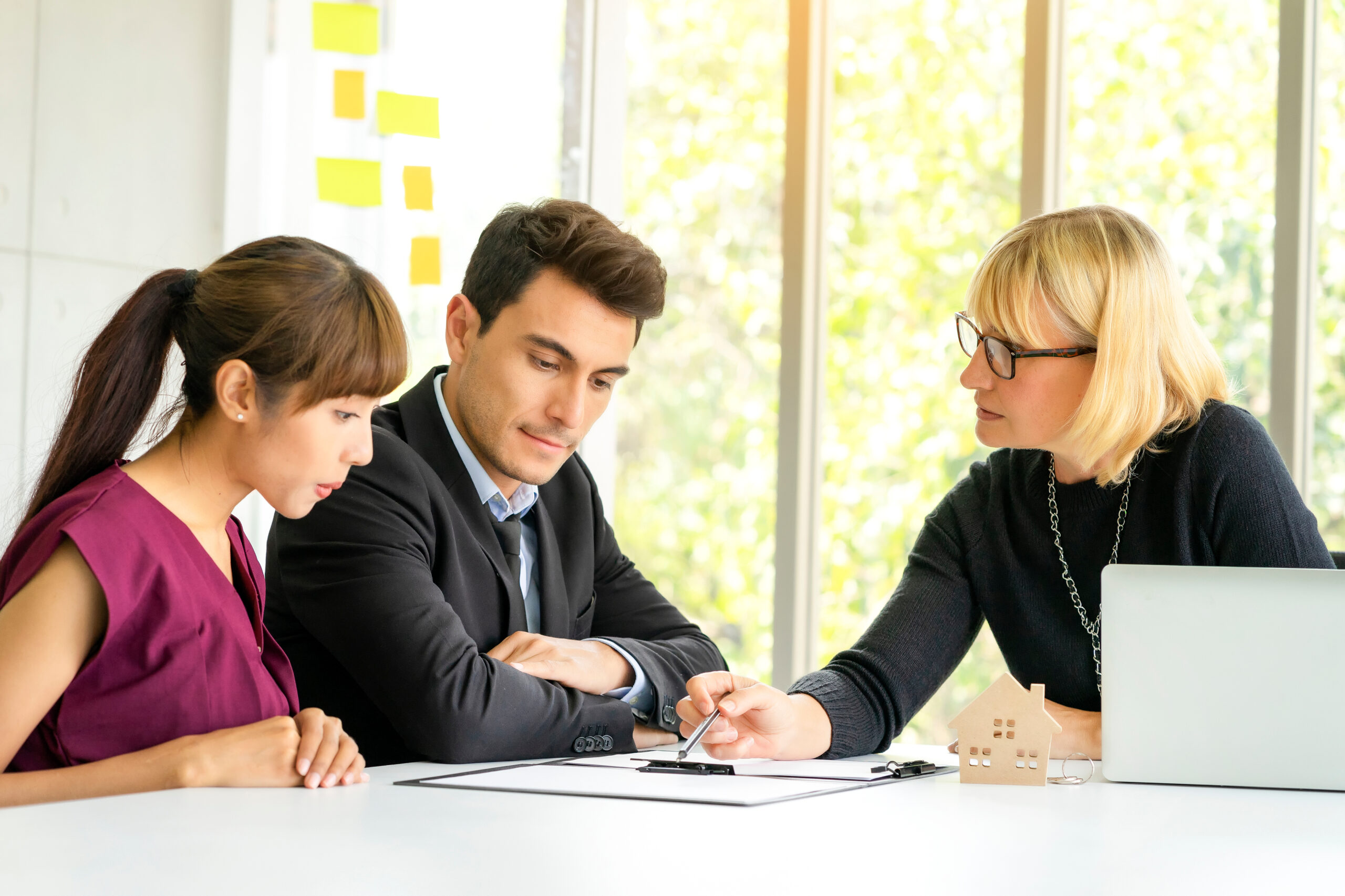 Loan officer reviewing a mortgage pre-approval letter with a young couple at a desk, walking through the renewal process before the letter expires.