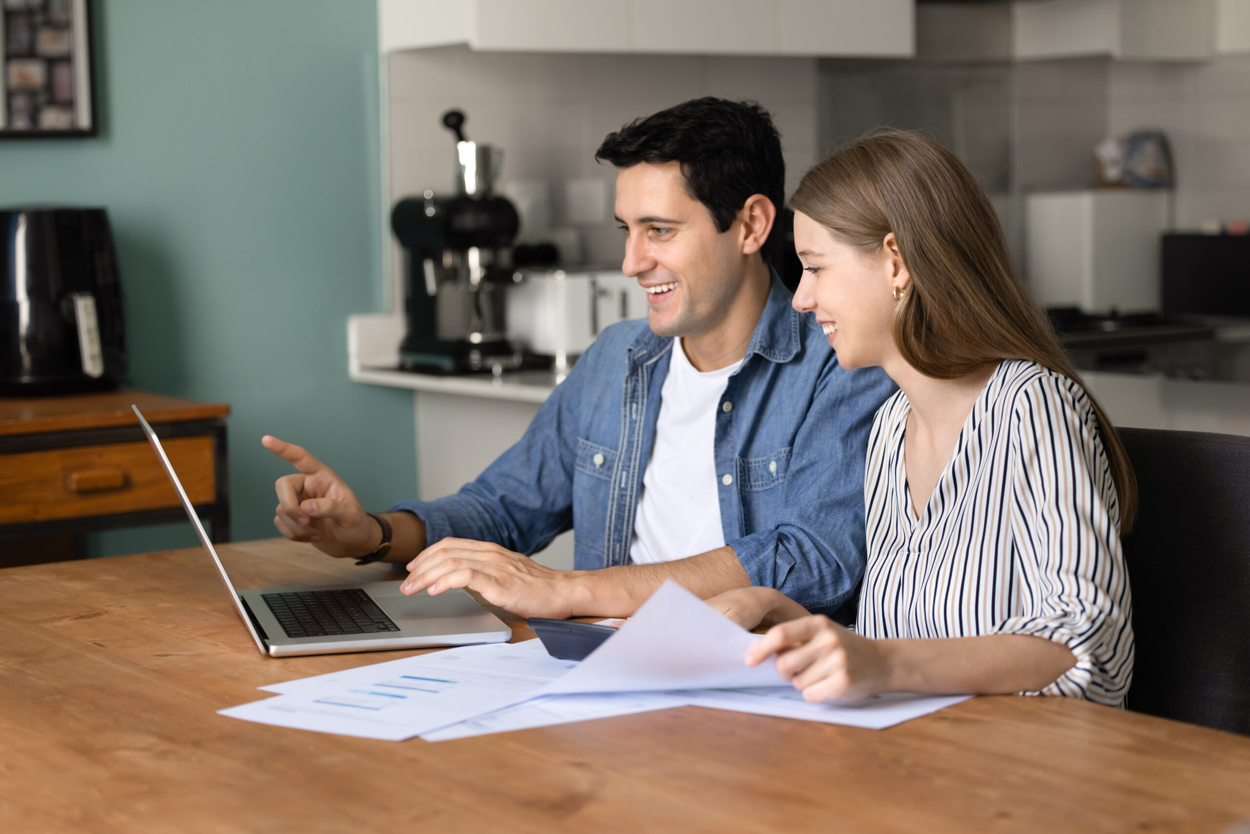 Contact Us image by Fellowship Home Loans Couple at a kitchen table reviewing mortgage Loan Estimates and lender paperwork on a laptop and printed documents during a lender comparison.