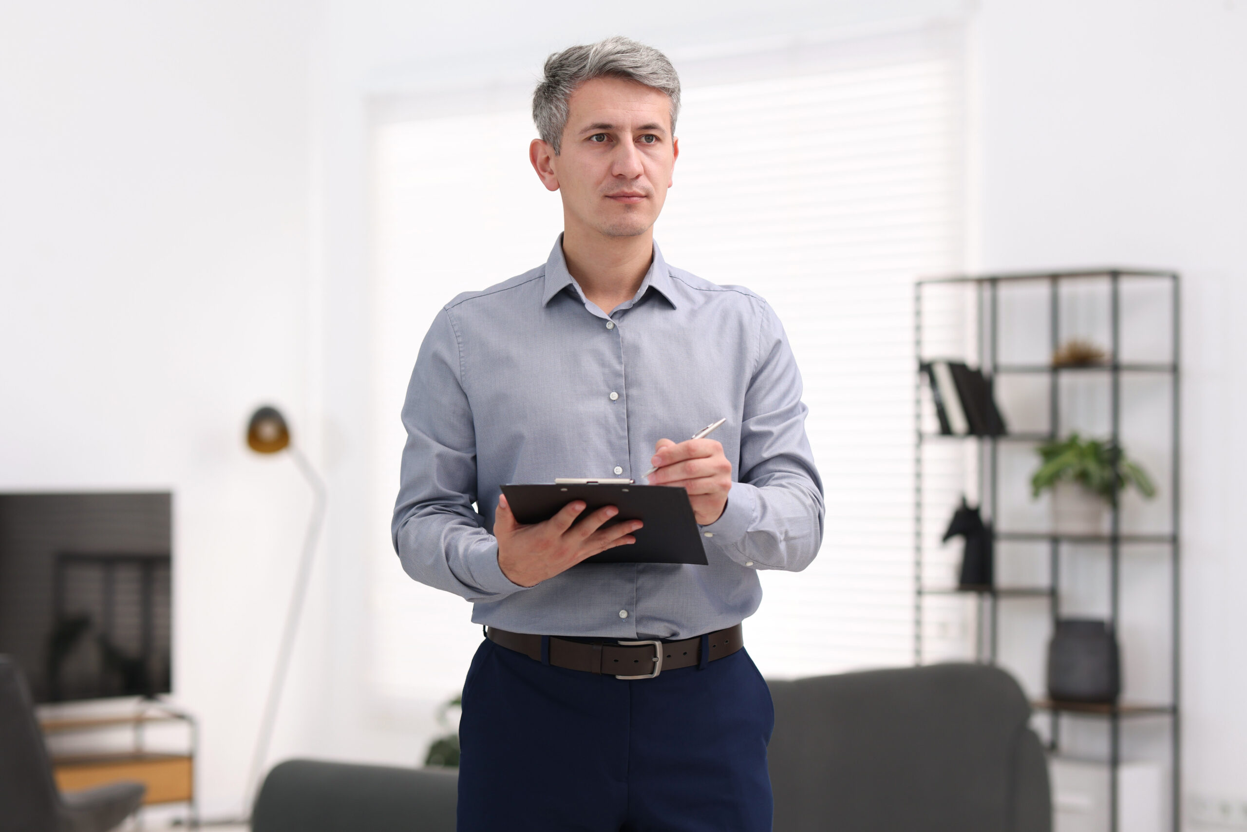 Real estate appraiser standing at the front entrance of a single-family home, holding a clipboard while conducting a property valuation walk-through.