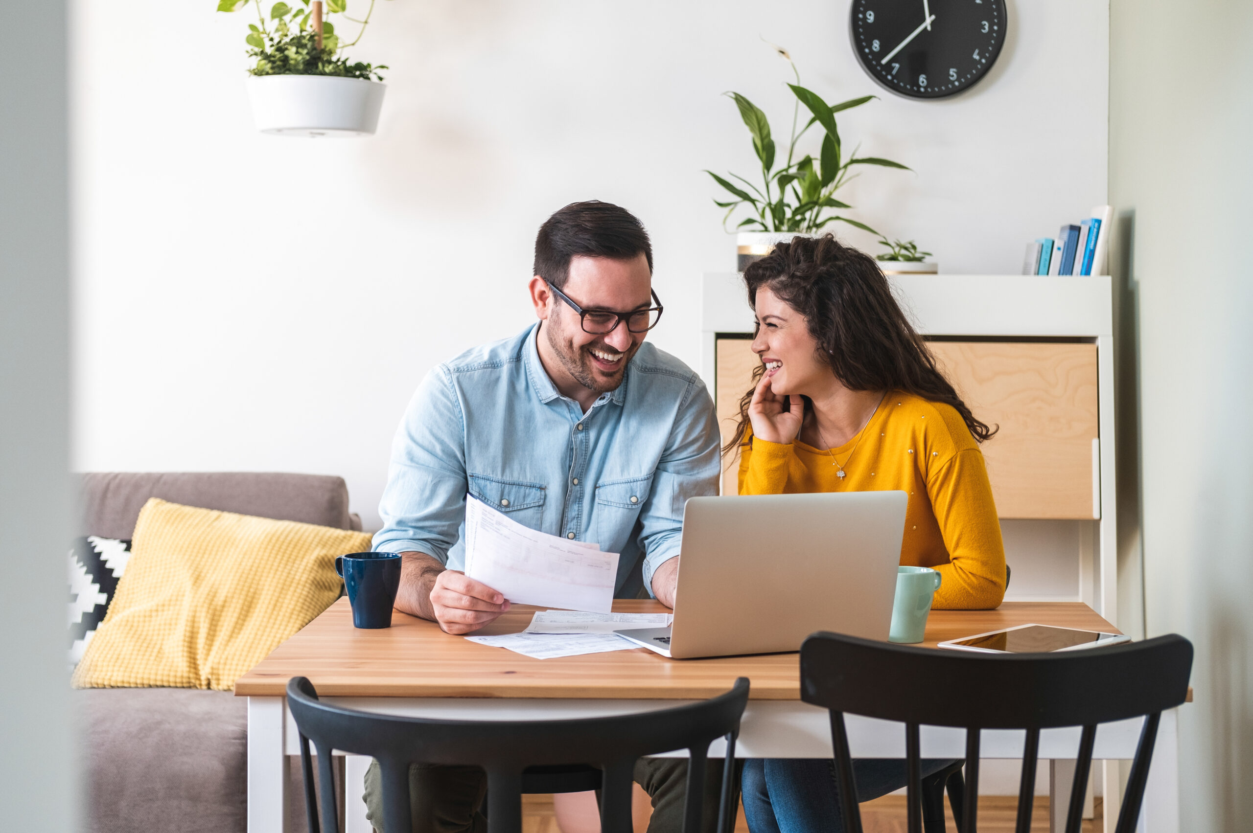 Contact Us image by Fellowship Home Loans Couple at a modern kitchen reviewing financial news on a laptop with a calculator while comparing mortgage rate notes.