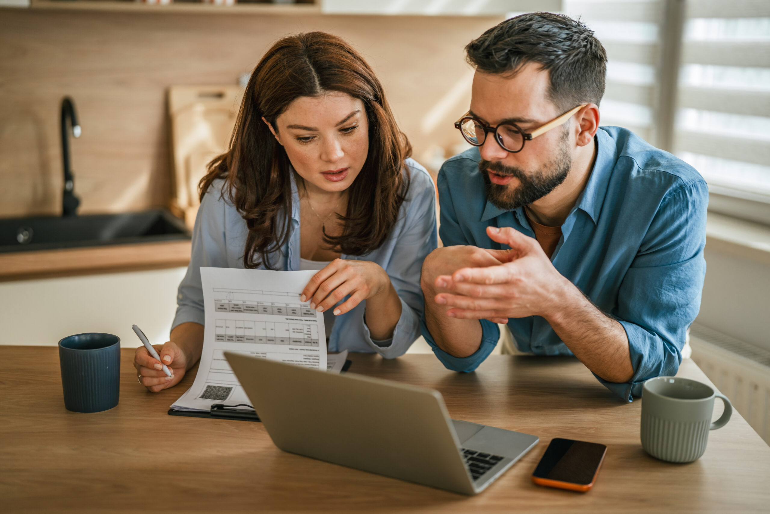 Couple at a kitchen table reviewing printed mortgage documents and a property tax bill while comparing escrow options side by side.