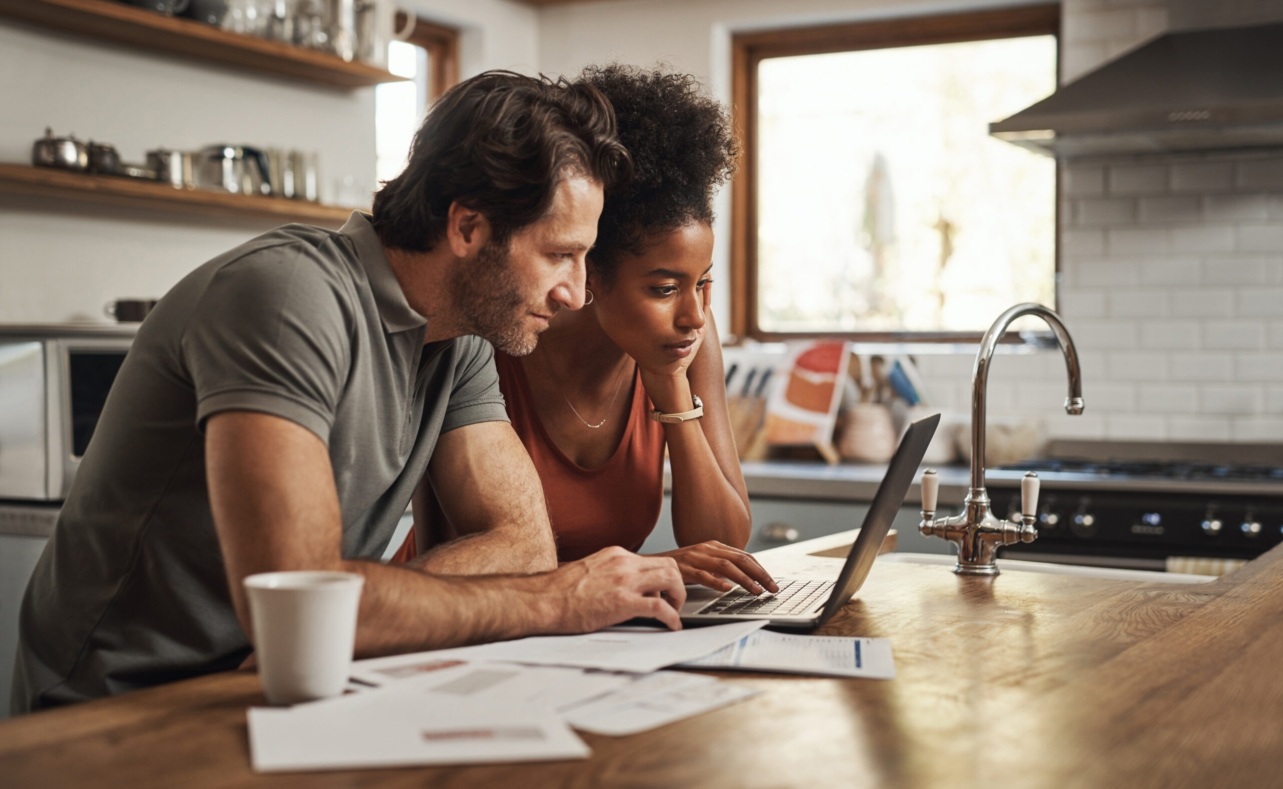 Couple at a kitchen counter reviewing printed mortgage paperwork and budget documents side by side, weighing how a down payment assistance program would pair with their loan.