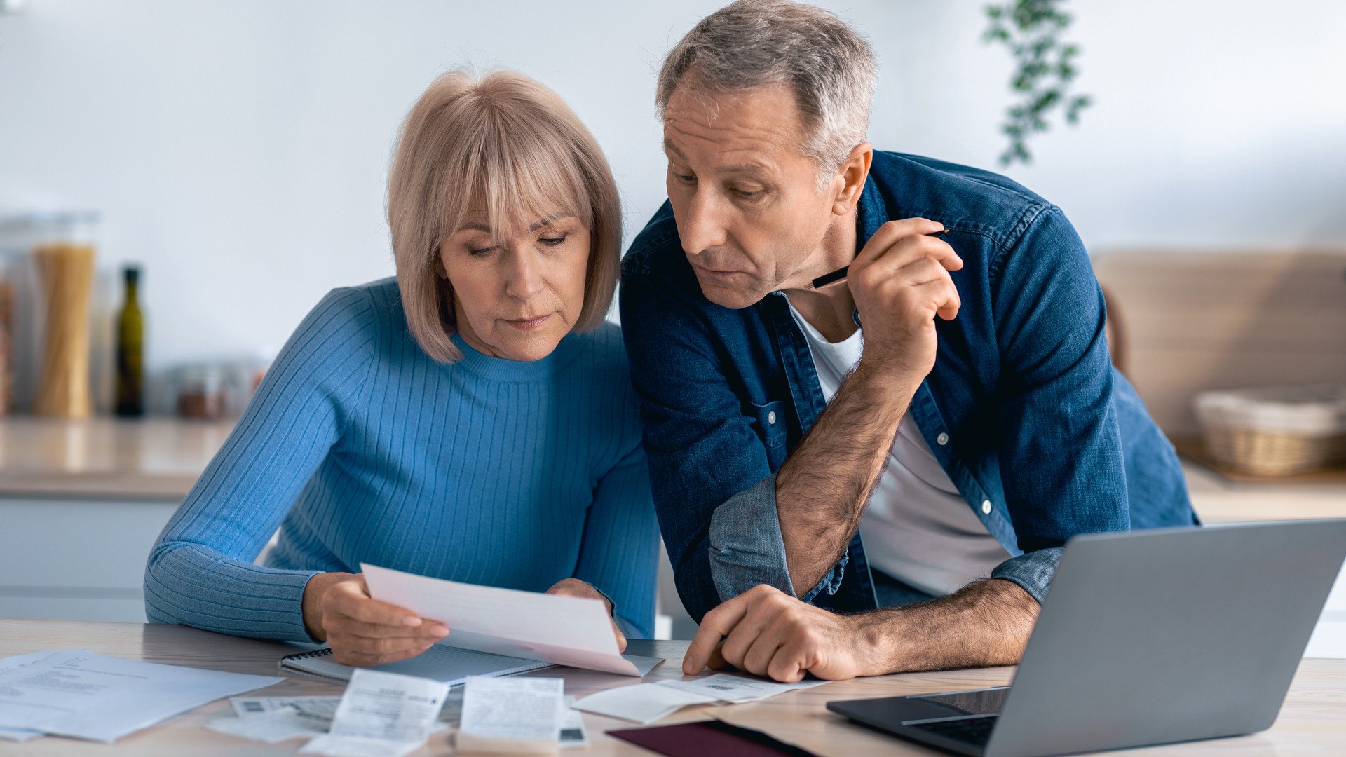 Contact Us image by Fellowship Home Loans Couple at a kitchen table reviewing homeowners insurance paperwork and a laptop quote during pre-approval prep, calculator and receipts on the table.