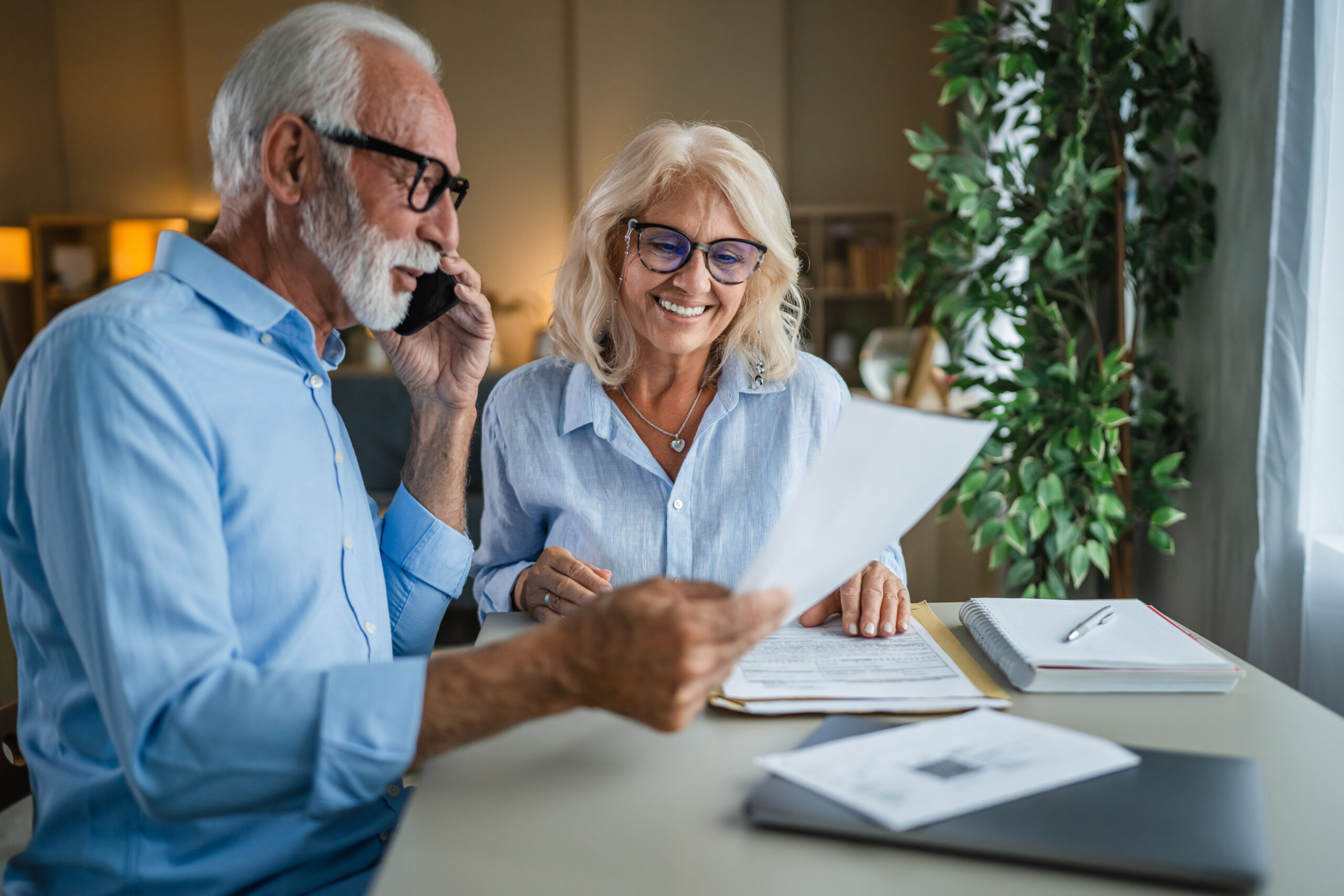 Contact Us image by Fellowship Home Loans Veteran homeowner couple seated at home using a phone to call their mortgage loan servicer about hardship-assistance options, representing the borrower's first step toward the new VA partial claim program for veterans behind on a VA home loan.