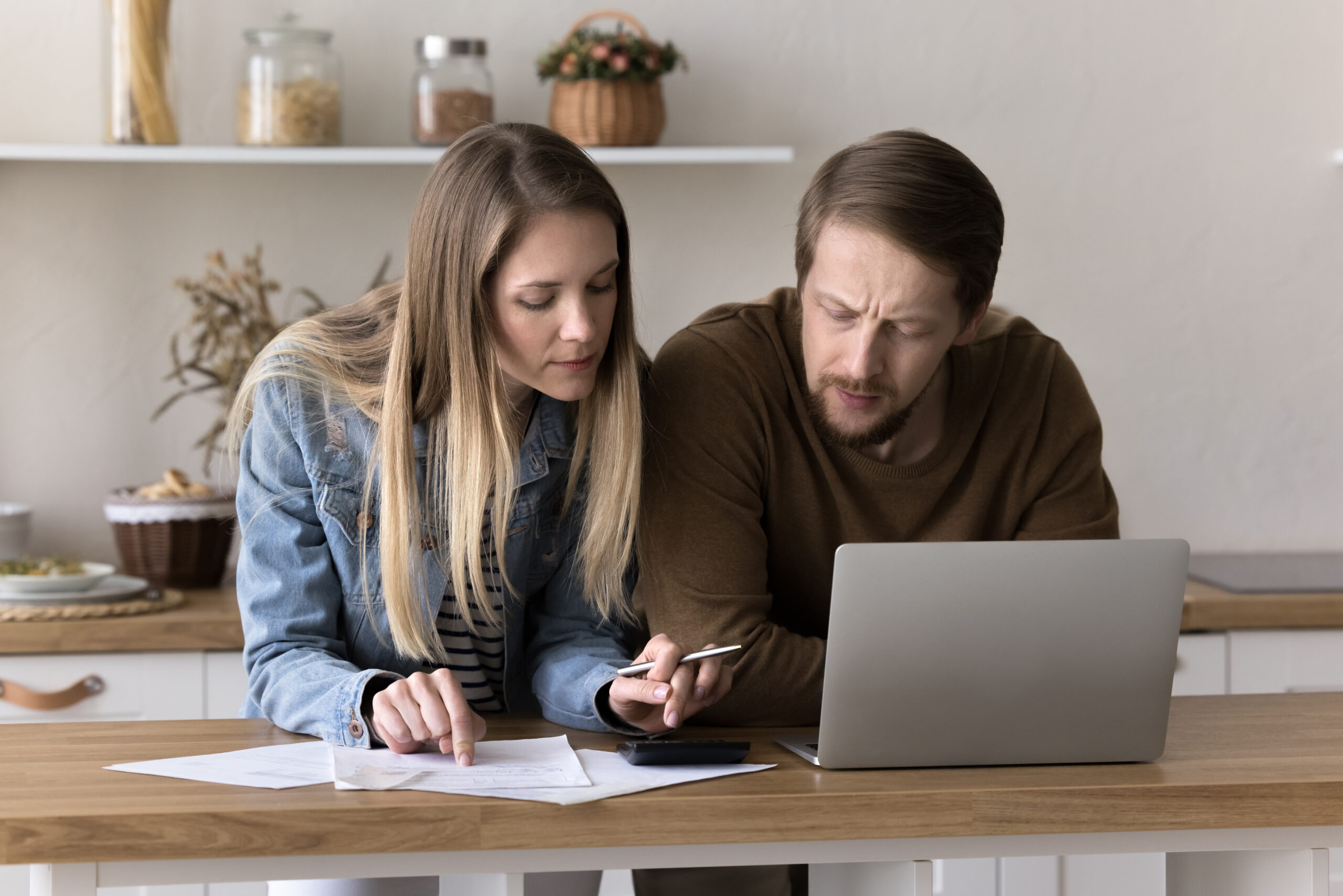 A young couple reviews a mortgage payment schedule with a calculator and documents at their kitchen table, weighing a 2-1 buydown offer on a home loan.