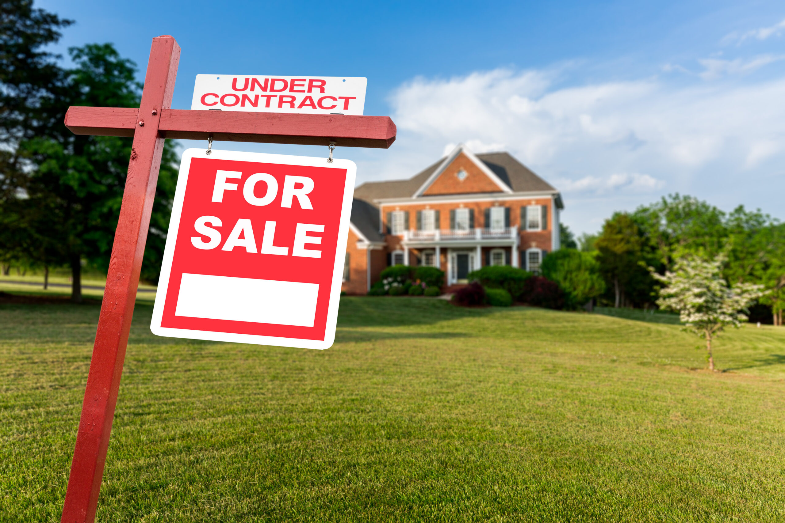 Red For Sale yard sign with an Under Contract rider on the lawn of a two-story American brick colonial home