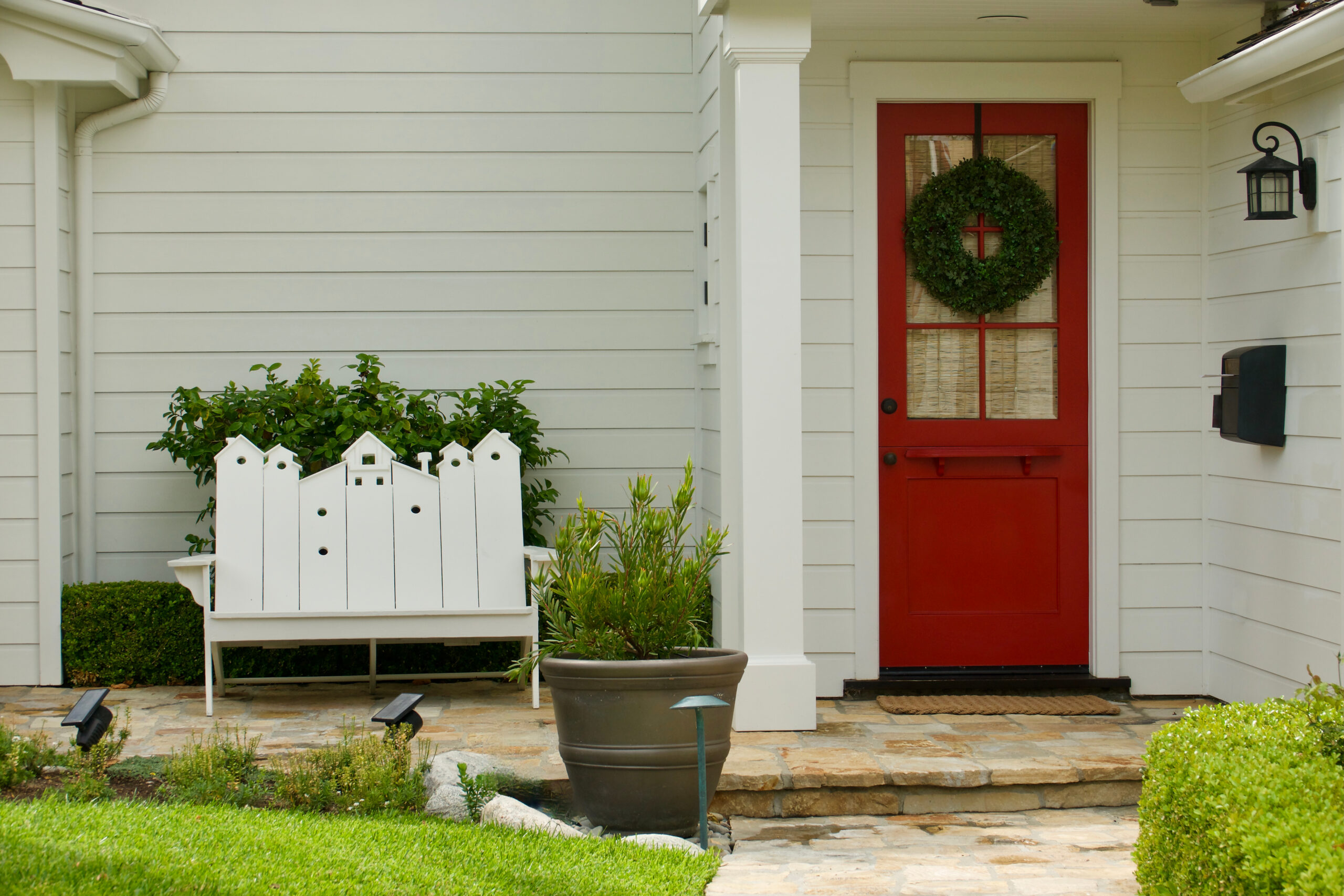 Front entrance of an American home with white lap siding, a columned porch and a red front door with a wreath