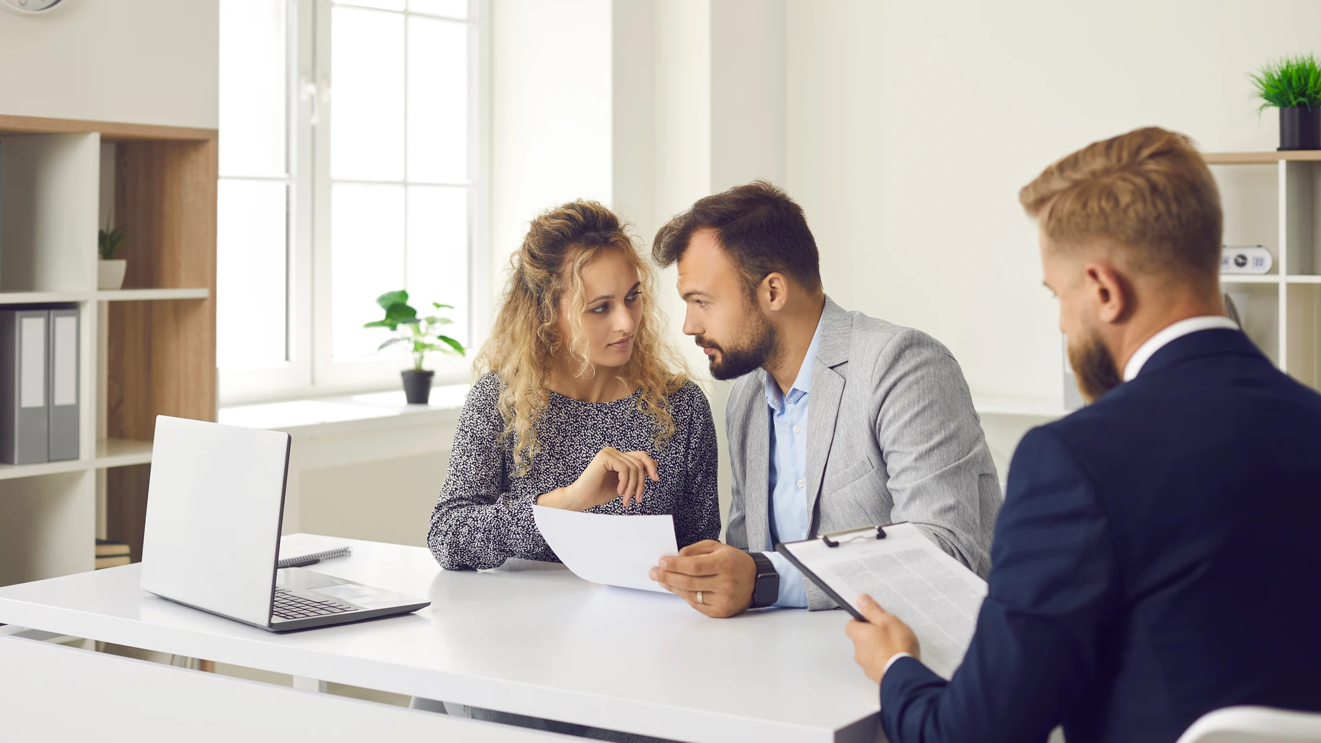 Couple reviewing a document together at a lender's desk while a loan advisor holds a clipboard