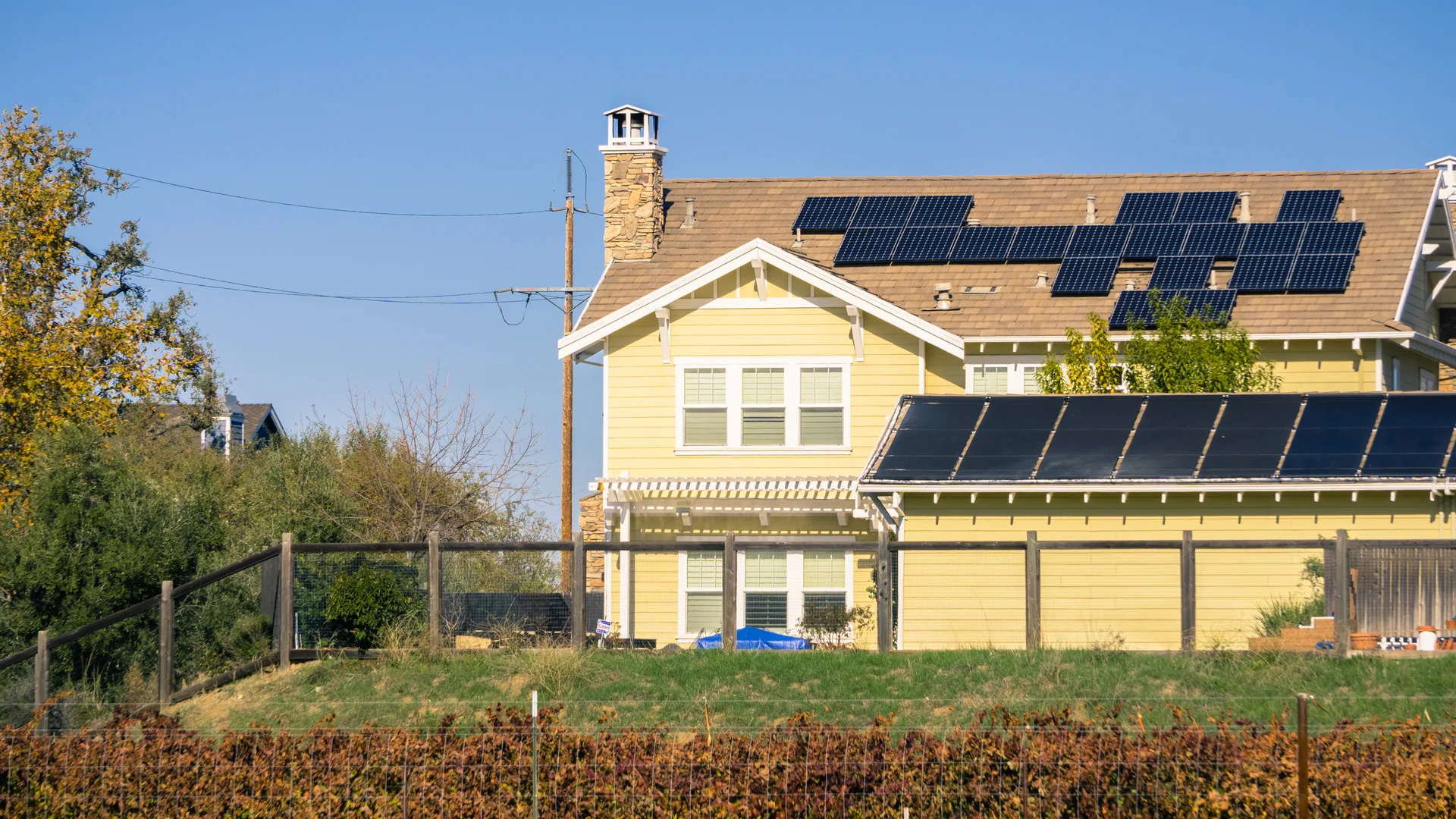 Contact Us image by Fellowship Home Loans A yellow craftsman-style house with rows of dark solar panels covering two sections of its shingled roof, seen past a wood fence